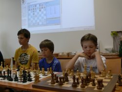 Vítěz Dětského dne Jan Beneš (vpravo za elektronickou šachovnicí), vedle Vojtěch Vincíbr a Vojtěch Koubík.